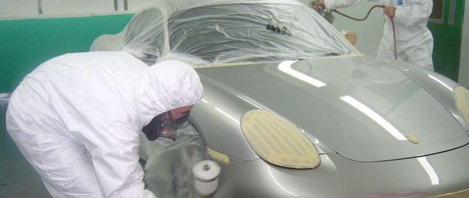Body shop technician in protective overalls preparing a car for spray painting