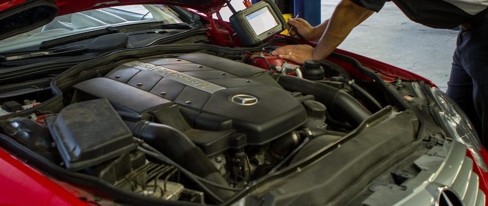 Technician connecting a diagnostic tablet to the engine of a red Mercedes